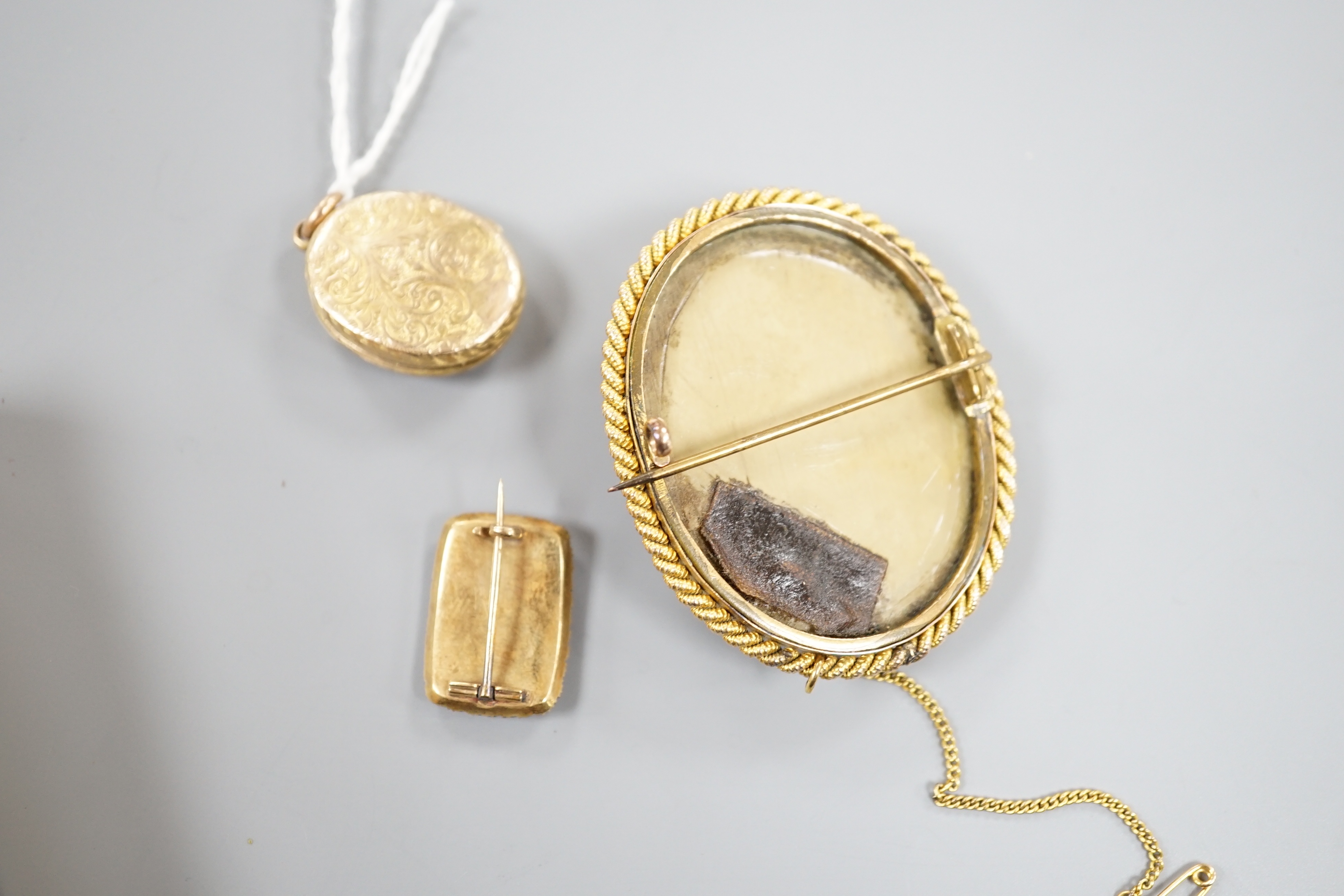 A 19th century yellow metal, seed pearl and plaited hair set mourning brooch, 20mm, a yellow metal oval locket and a mounted lava brooch.